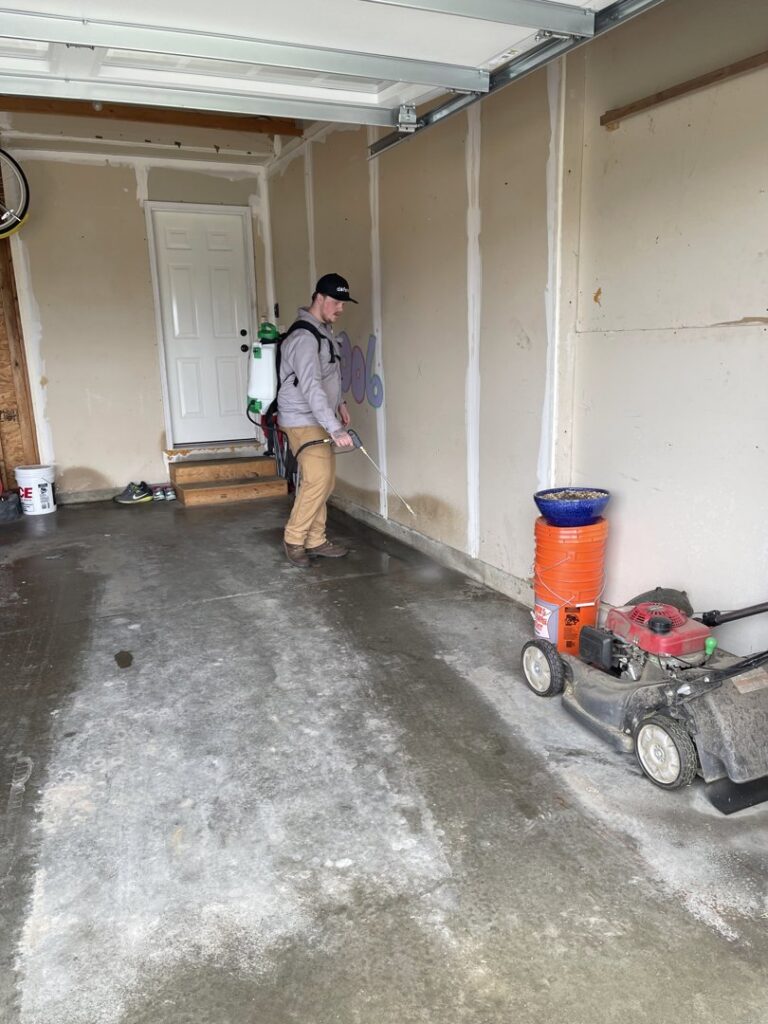 A pest control technician spraying a garage wall with a backpack sprayer for Defend Pest Solutions in Sioux Falls, SD.