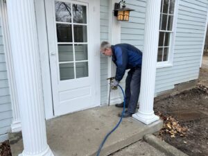 A pest control technician spraying the exterior entry point of a house during a pest treatment by EcoPro Termite & Pest in Dayton, OH