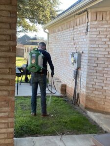 A pest control technician from Blue Line Pest Police spraying the exterior of a house in Fort Worth, TX.