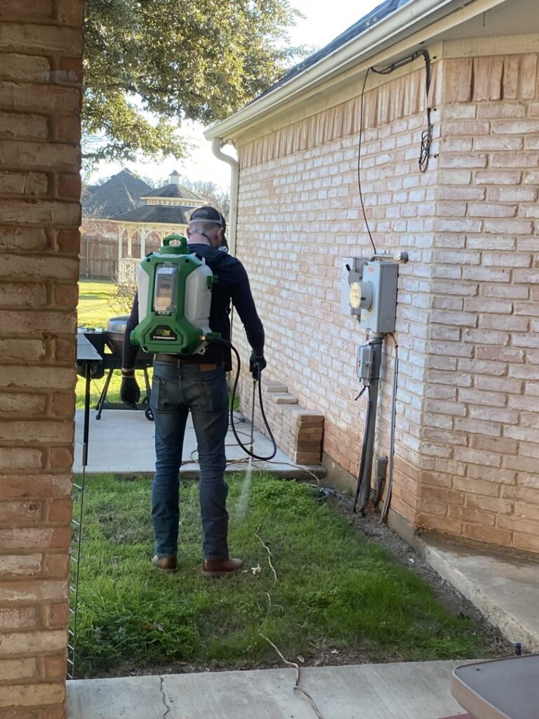 A pest control technician from Blue Line Pest Police spraying the exterior of a house in Fort Worth, TX.