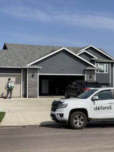 A pest control technician spraying the exterior of a house with a backpack sprayer for Defend Pest Solutions in Sioux Falls, SD.