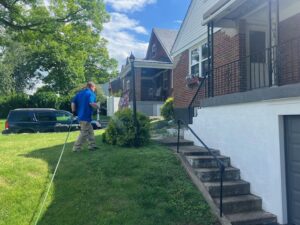 A pest control technician spraying the exterior of a residential house during a treatment by EcoPro Termite & Pest in Dayton, OH