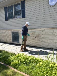 A pest control technician from JAMPestControl spraying the exterior foundation of a house in Dickinson, ND.