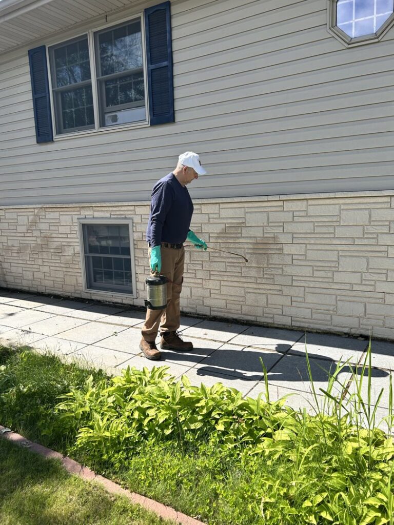 A pest control technician from JAMPestControl spraying the exterior foundation of a house in Dickinson, ND.