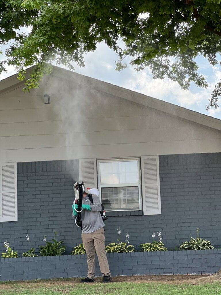A Mosquito Malone Pest Control technician applying a mist treatment to a house exterior in Edmond, OK.
