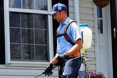 A pest control technician using a backpack sprayer to treat the exterior of a residential house by Norman Pest Control in Norman, OK.