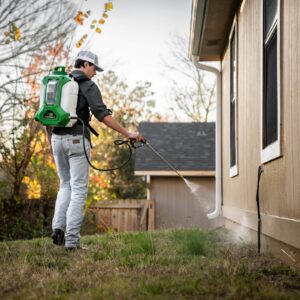 A pest control technician using a backpack sprayer to treat the exterior of a house for Ozark Pest Control in Fayetteville, AR.