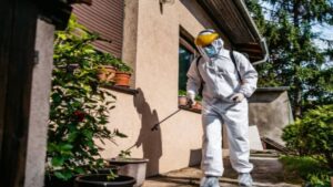 A pest control technician in a protective suit spraying the exterior of a house for TOTAL Exterminating Co. Inc. in Indianapolis, IN.