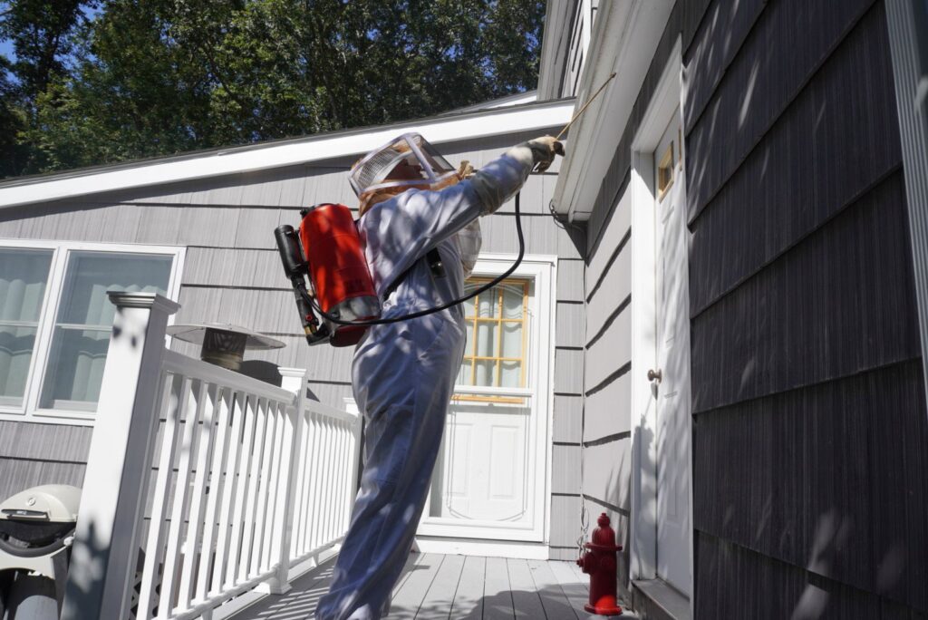 A Catseye Pest Control technician in a protective suit spraying the exterior of a house in Hartford, CT.