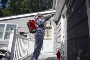 A Catseye Pest Control technician in a protective suit spraying the exterior of a house in Hartford, CT.