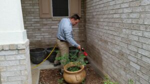 A pest control technician spraying the foundation and exterior wall of a house for pest treatment by Beeline Pest Control Texas in San Antonio, TX.