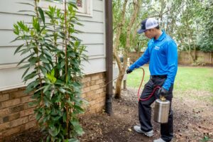 A Pest Authority technician applying pest control treatment to the foundation of a residential home in Dover, DE.