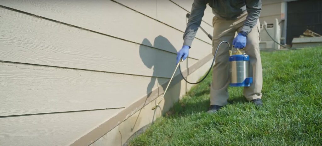 A pest control technician spraying the foundation of a house for pest prevention at Richmond Pest Control in Richmond, KY.