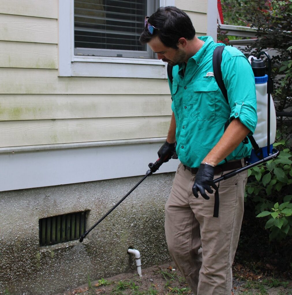 A pest control technician spraying the foundation of a house during a treatment by Spartina Pest Management in Port Royal, SC.