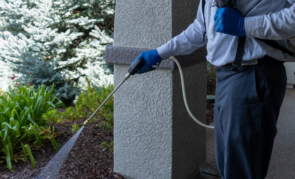 A pest control technician from The Noble Way Pest Control spraying along a house foundation in Sacramento, CA.