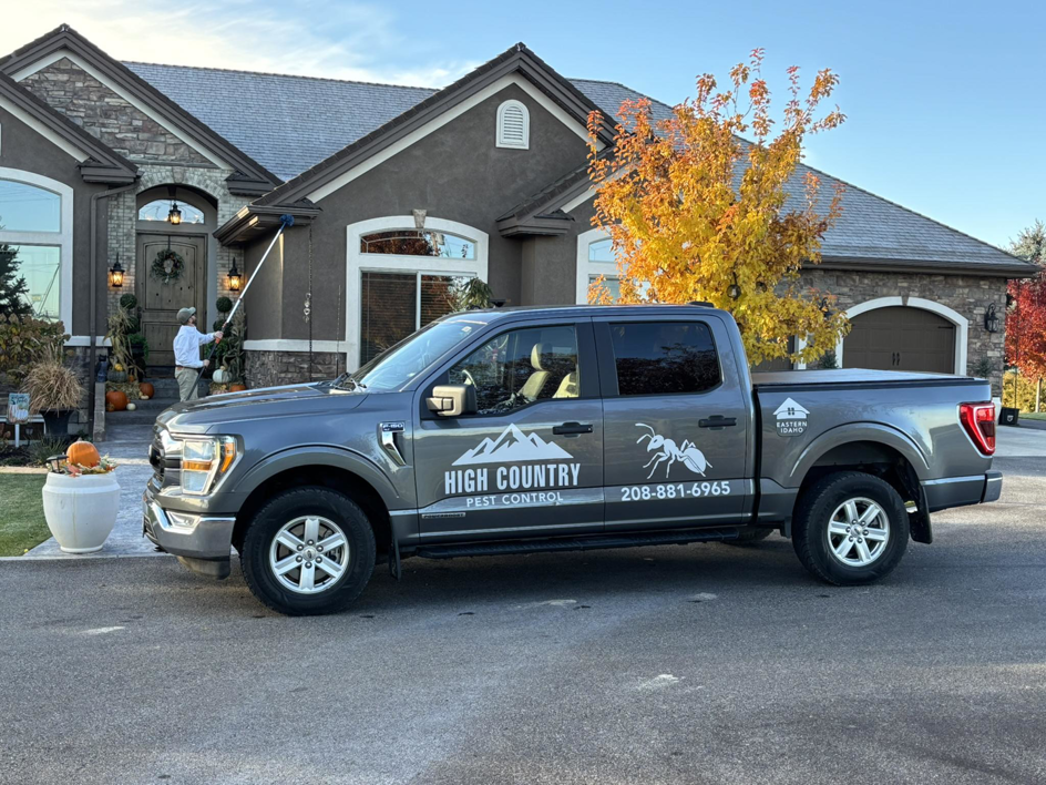 A pest control technician spraying the exterior of a house from a High Country Pest Control truck in Colorado Springs, CO.