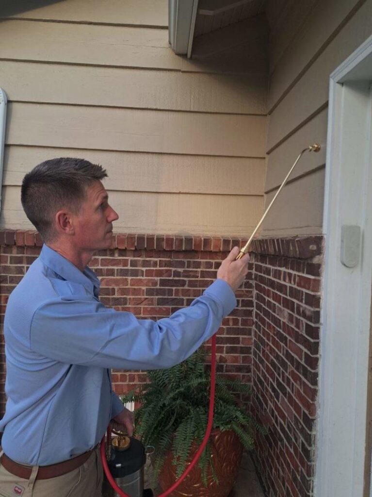 A Howe Pest Management technician in Manhattan, KS, spraying the exterior of a brick house for pest control.