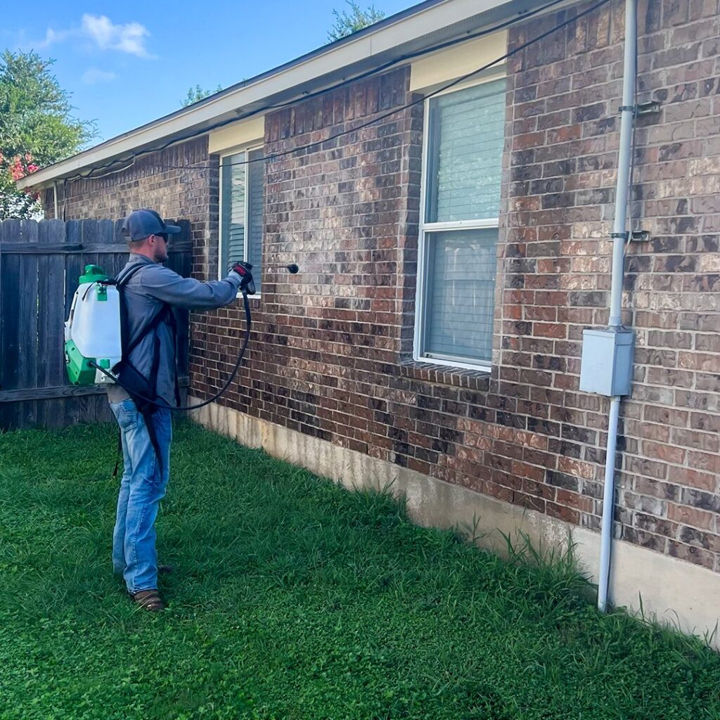 A pest control technician from Kaizen Pest Management spraying the exterior of a house in Austin, TX.
