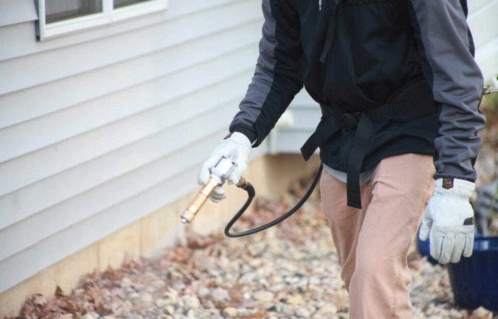 A pest control technician spraying the exterior of a house for pests at a job site for Modern Solutions Pest Control in Rockford, IL.