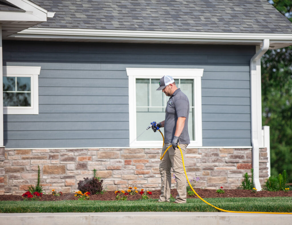 A pest control technician from Titan Pest Pro - Springfield spraying the perimeter of a residential house in Springfield, MO.