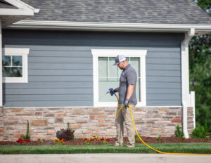 A pest control technician from Titan Pest Pro - Springfield spraying the perimeter of a residential house in Springfield, MO.