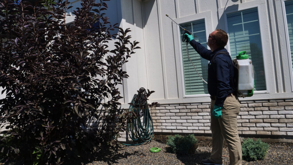 A Pestcom Pest Management technician applying pest control treatment to the exterior of a residential home in Nampa, ID
