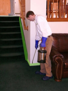 A pest control technician spraying indoors near a staircase for Saela Pest Control in Hubbard, OR.