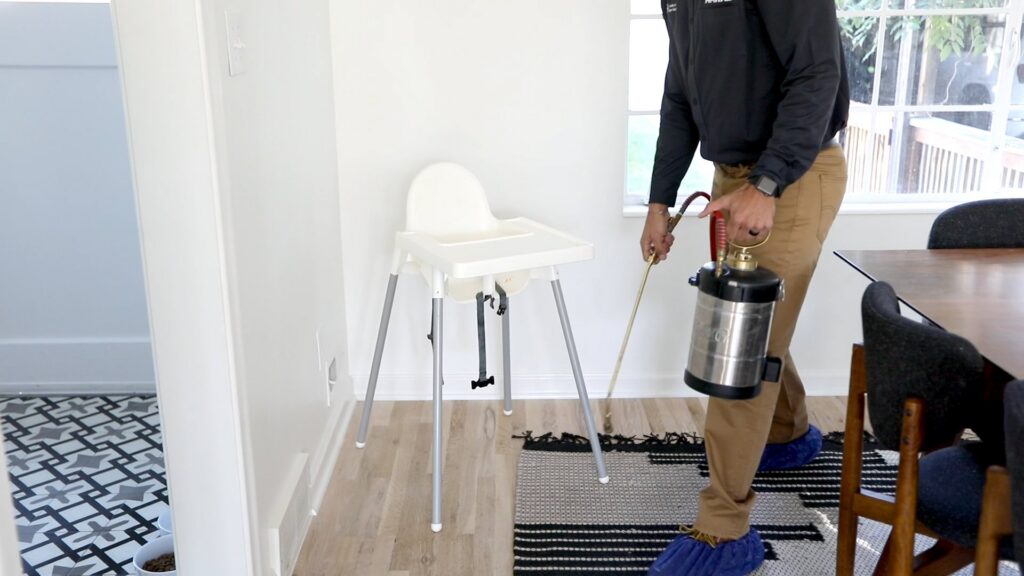 A Hawx Pest Control technician spraying inside a home near a high chair for pest treatment in San Antonio, TX.