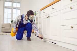 A pest control technician spraying under kitchen cabinets for Venum Pest Solutions in Fayetteville, NC.