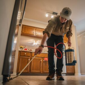 A pest control technician spraying along kitchen baseboards during an interior treatment by Ozark Pest Control in Fayetteville, AR.