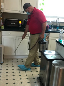 A pest control technician wearing a mask and shoe covers, spraying for pests inside a kitchen at Otho's Pest Management in Randleman, NC