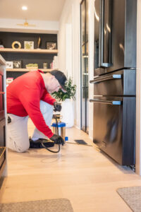 A pest control technician spraying behind a kitchen refrigerator for pest treatment by DOA Pest Service in Nashville, TN.