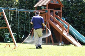 A pest control technician from Eco-Safe Pest Control spraying a lawn near a playground in Dallas, TX