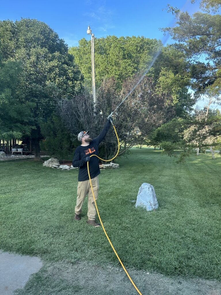 An Elite Pest Control technician spraying outdoor foliage for pest treatment in Maple Grove, MN.