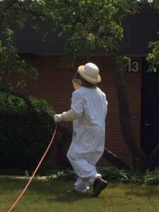 An ABG Pest Control services technician in a protective suit spraying outdoors in West Chicago, IL.