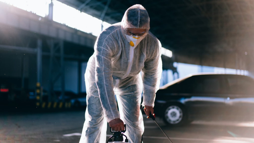 A pest control technician in a hazmat suit spraying outdoors for pest control by Hub City Pest Control in Jackson, TN