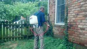 A pest control technician performing a perimeter spray treatment around a house for Out A Site Pest Control in Cincinnati, OH