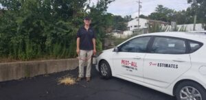A pest control technician holding a sprayer next to a company car for Pest-All Exterminating Co. in Cincinnati, OH.