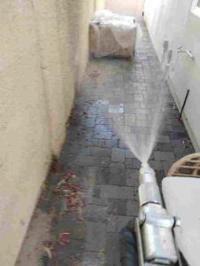 A pest control technician spraying pesticide along a paved walkway next to a building wall, providing service for Bernard's Pest in Glendale, AZ.