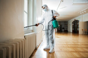 A pest control technician in a protective suit spraying a radiator, performing pest treatment for SWAT It Pest Control in Tempe, AZ.