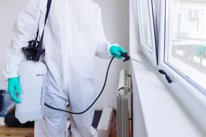 A pest control technician in a protective suit spraying near a window at a property serviced by Habitat Pest Control in San Jose, CA.