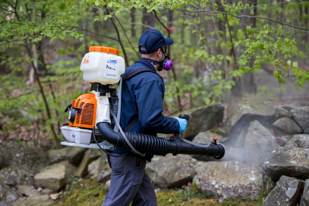 A pest control technician spraying a wooded area for pests at Big Blue Bug Solutions in Providence, RI