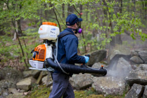 A pest control technician spraying a wooded area for pests at Big Blue Bug Solutions in Providence, RI