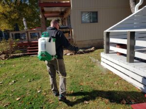 A pest control technician spraying the yard around a residential home for Quit Buggin' Me Pest Control in Owasso, OK.