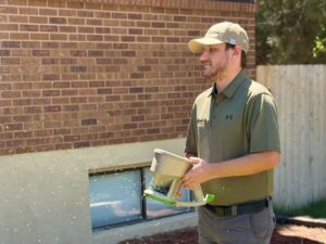 A pest control technician from Gravity Pest Control spreading pest control granules near a home's foundation in Caldwell, ID.