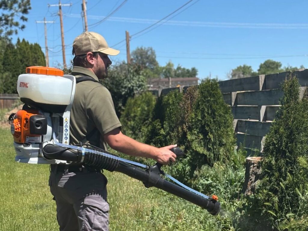 A pest control technician from Gravity Pest Control treating bushes and foliage with a backpack sprayer in Caldwell, ID.