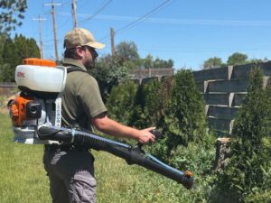A pest control technician from Gravity Pest Control treating bushes and foliage with a backpack sprayer in Caldwell, ID.