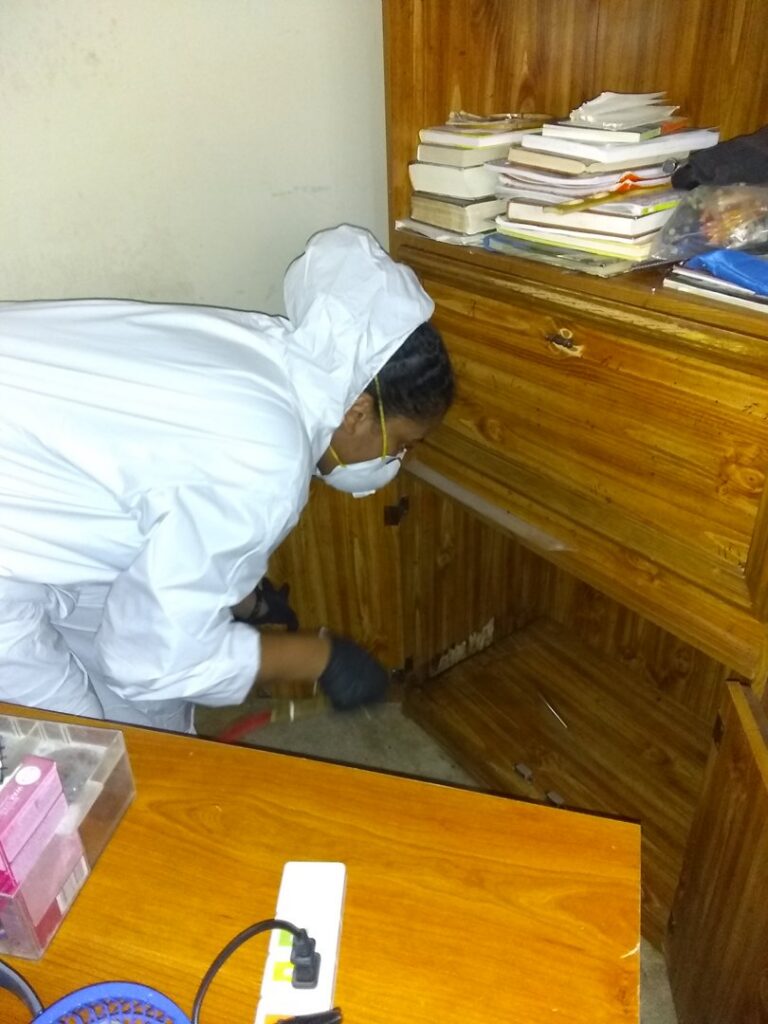 A pest control technician in a hazmat suit treating inside a wooden cabinet for pests at a client's location in Knoxville, TN.