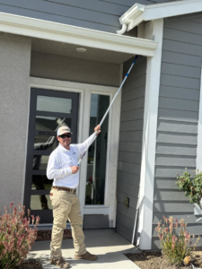 A Carreon Pest Control technician using a long pole to treat the eaves of a house in Bakersfield, CA.