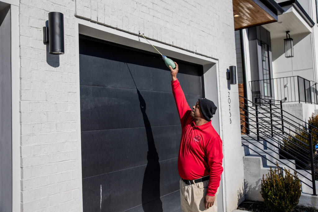 A pest control technician treating the exterior of a garage door with an applicator for DOA Pest Service in Nashville, TN.